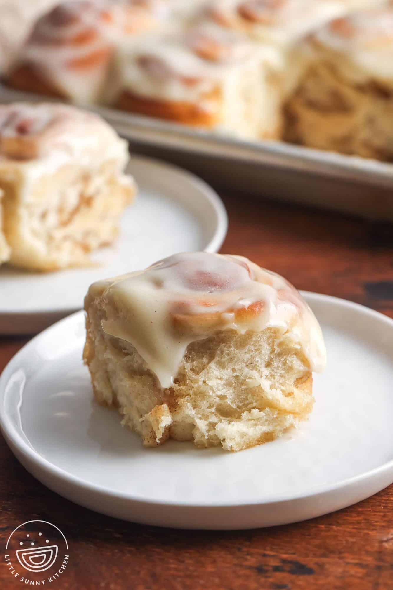 one mini cinnamon roll with icing on a small white plate, set on a wooden table.