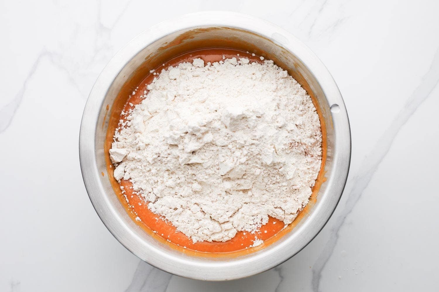 Flour mixture poured on top of pumpkin batter in a bowl.