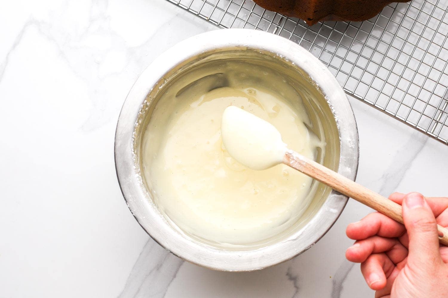 Hand stirring cream cheese glaze in a mixing bowl with a spatula.