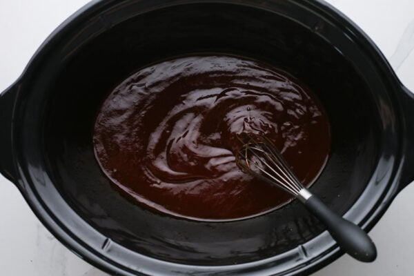 barbecue sauce at the bottom of a slow cooker, stirred with a whisk.
