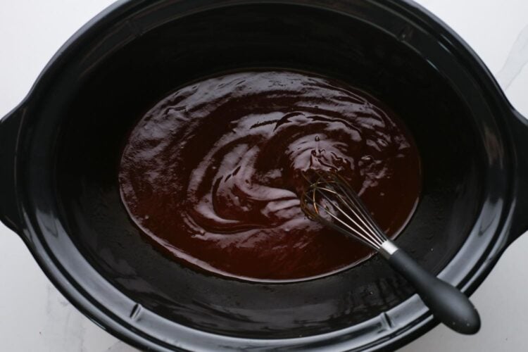 barbecue sauce at the bottom of a slow cooker, stirred with a whisk.