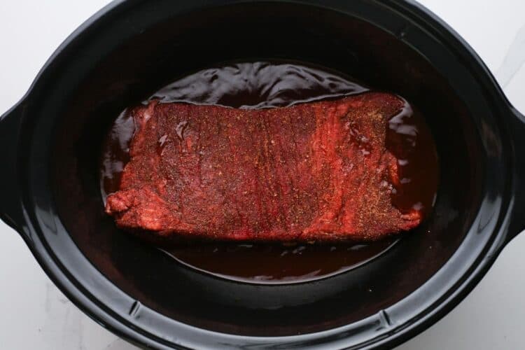 seasoned brisket on top of bbq sauce in a slow cooker