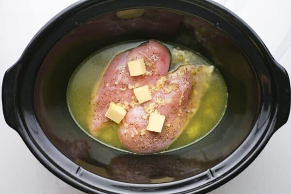 butter, garlic, broth, and raw chicken, in a slow cooker.