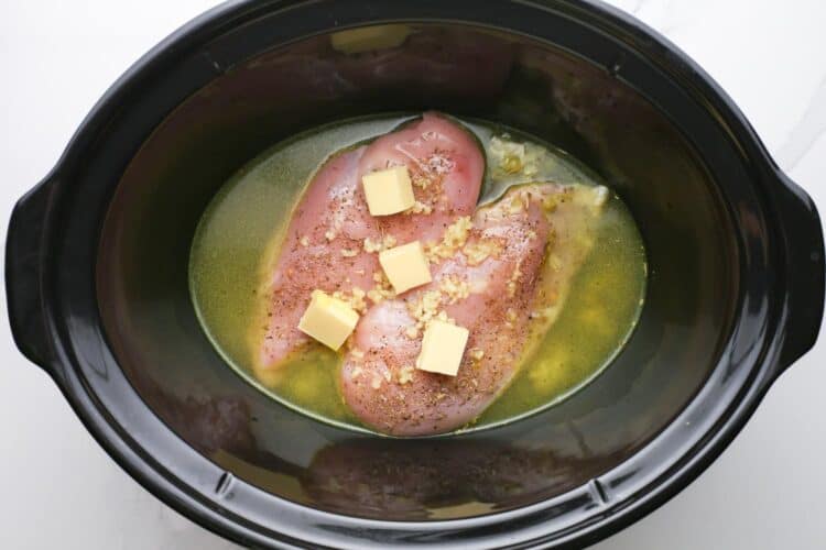 butter, garlic, broth, and raw chicken, in a slow cooker.