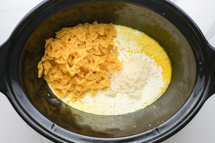 bowtie pasta, parmesan cheese, and cream added to a crockpot.