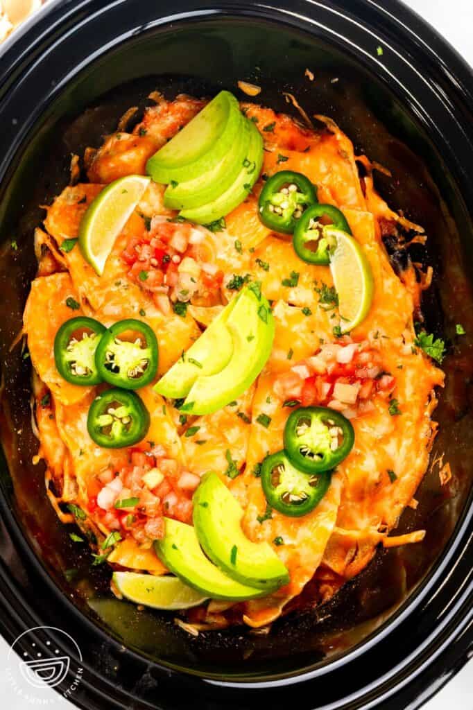 crockpot chicken enchiladas casserole topped with pico de gallo, jalapenos, and sliced avocado.