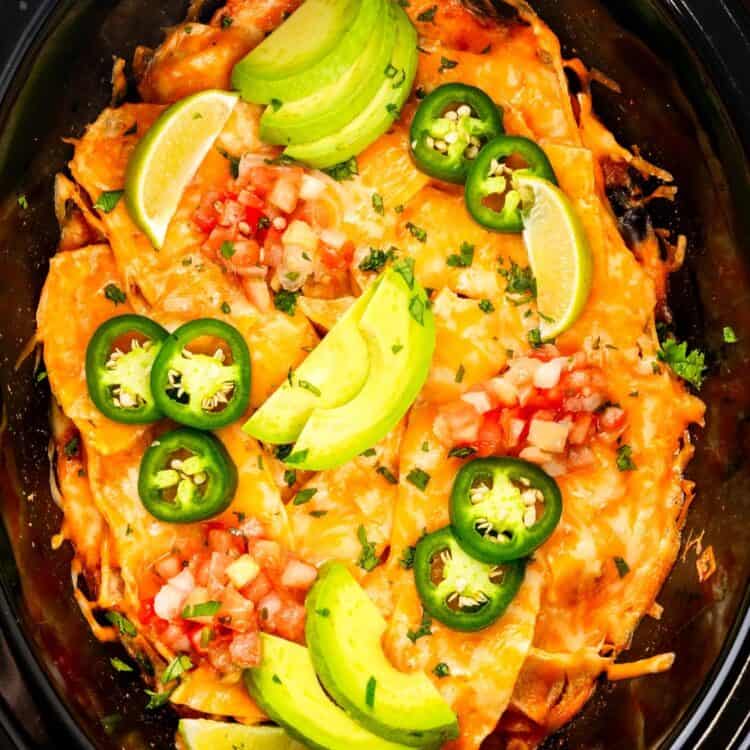 crockpot chicken enchiladas casserole topped with pico de gallo, jalapenos, and sliced avocado.