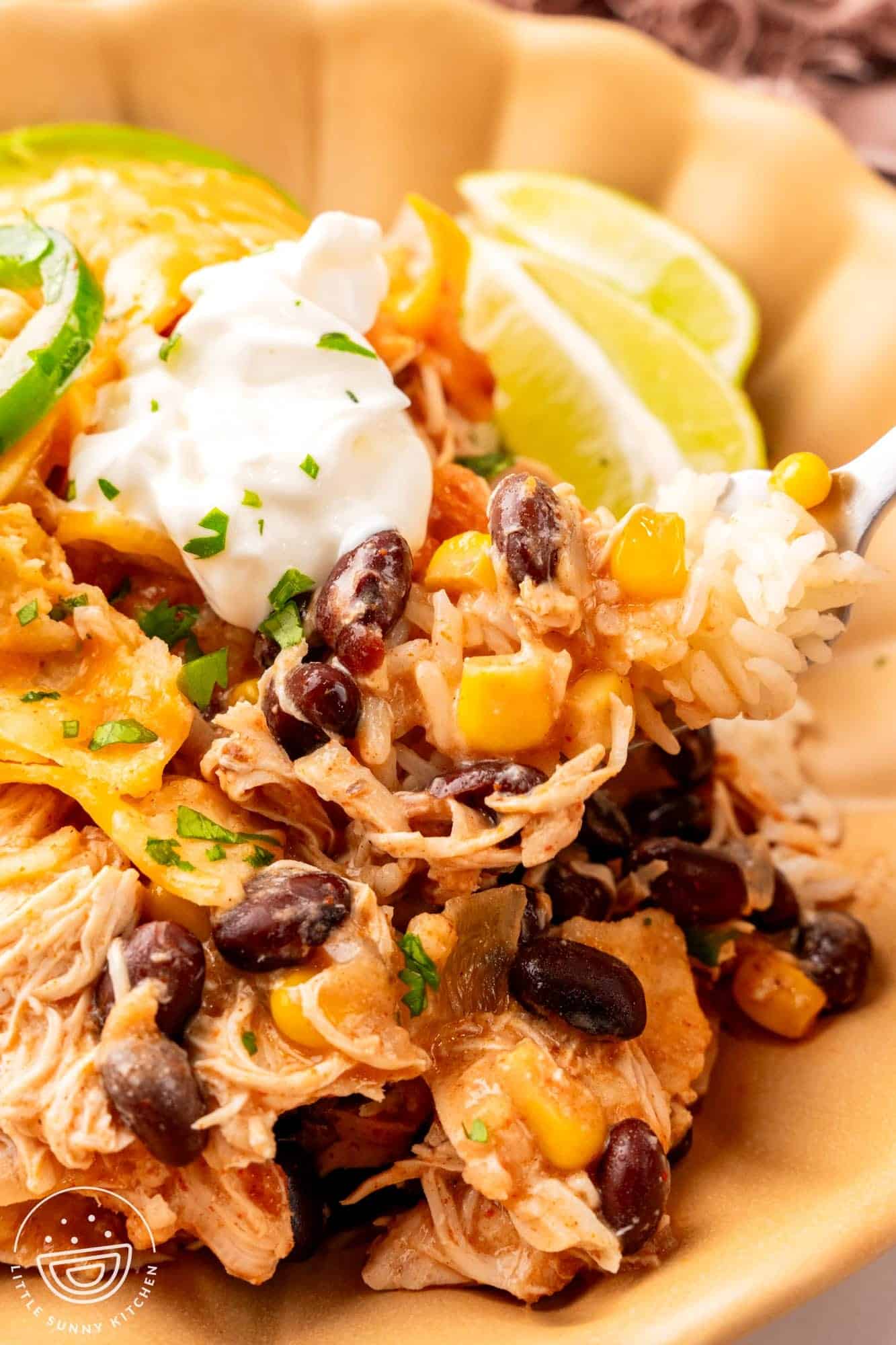 chicken enchilada casserole in a bowl with rice, garnished with fresh lime wedges and sour cream.