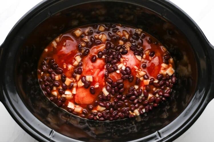 Overhead shot of a slow cooker with chicken, beans, and red sauce before cooking.