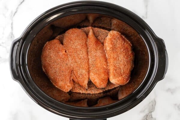 four seasoned chicken breasts in a slow cooker.