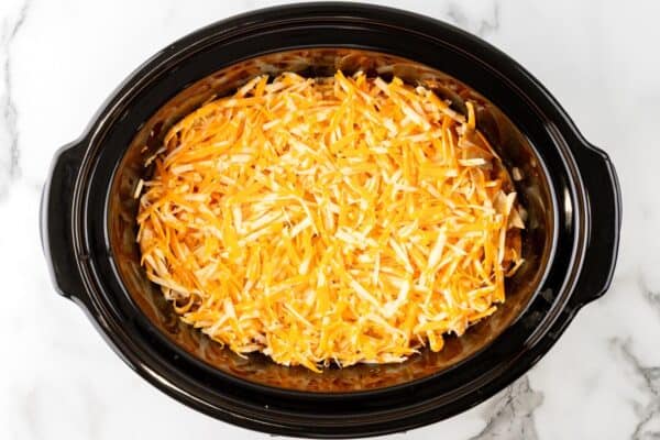 shredded colby jack cheese topping enchilada casserole in a crock pot.