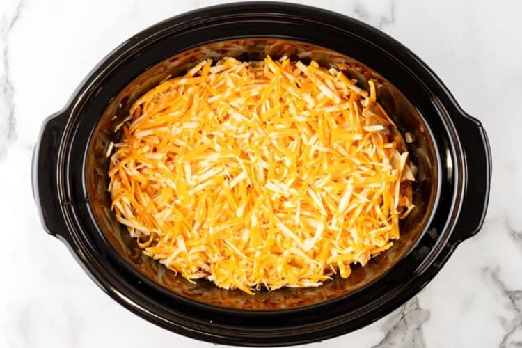 shredded colby jack cheese topping enchilada casserole in a crock pot.