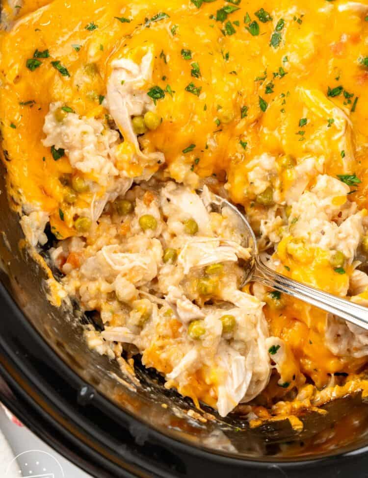 a crock pot of chicken rice casserole. A spoon is scooping up a serving.