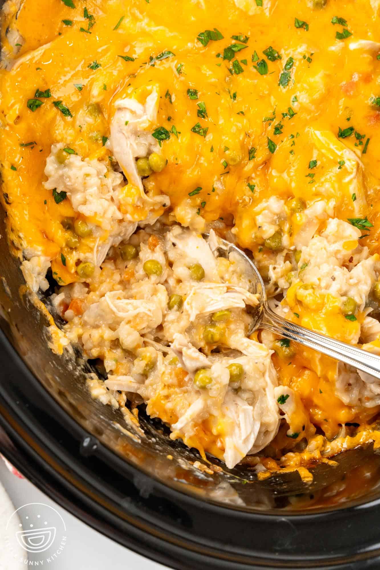 a crock pot of chicken rice casserole. A spoon is scooping up a serving.