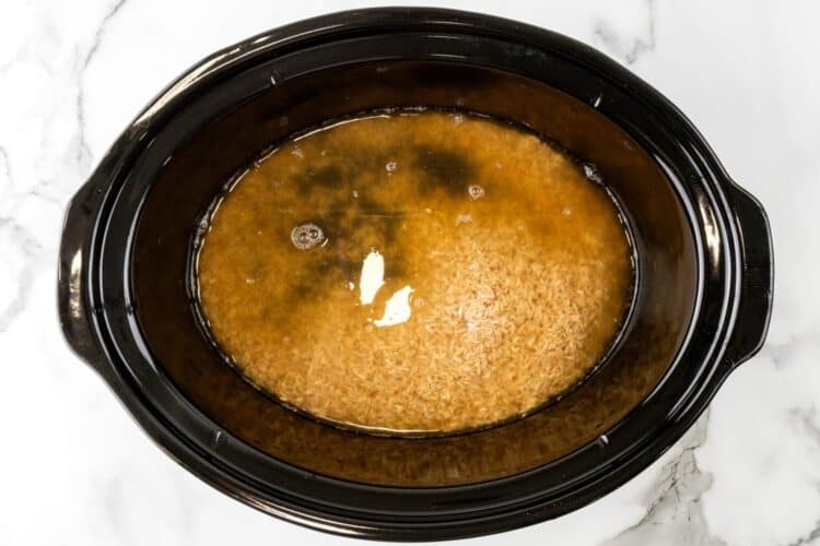 brown rice and chicken stock in a black slow cooker, viewed from overhead.