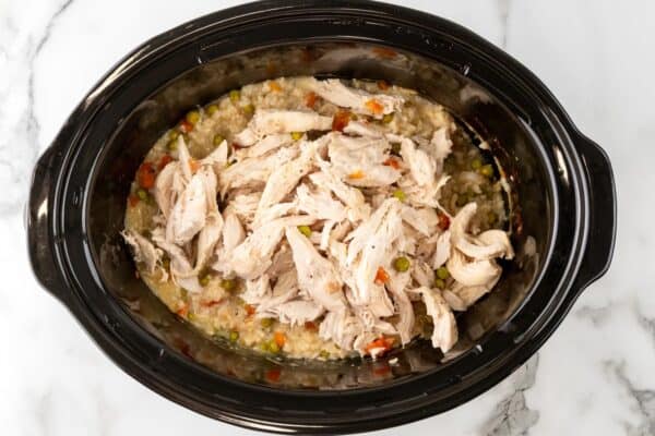 shredded chicken added to a crock pot of brown rice and veggies to make a casserole.