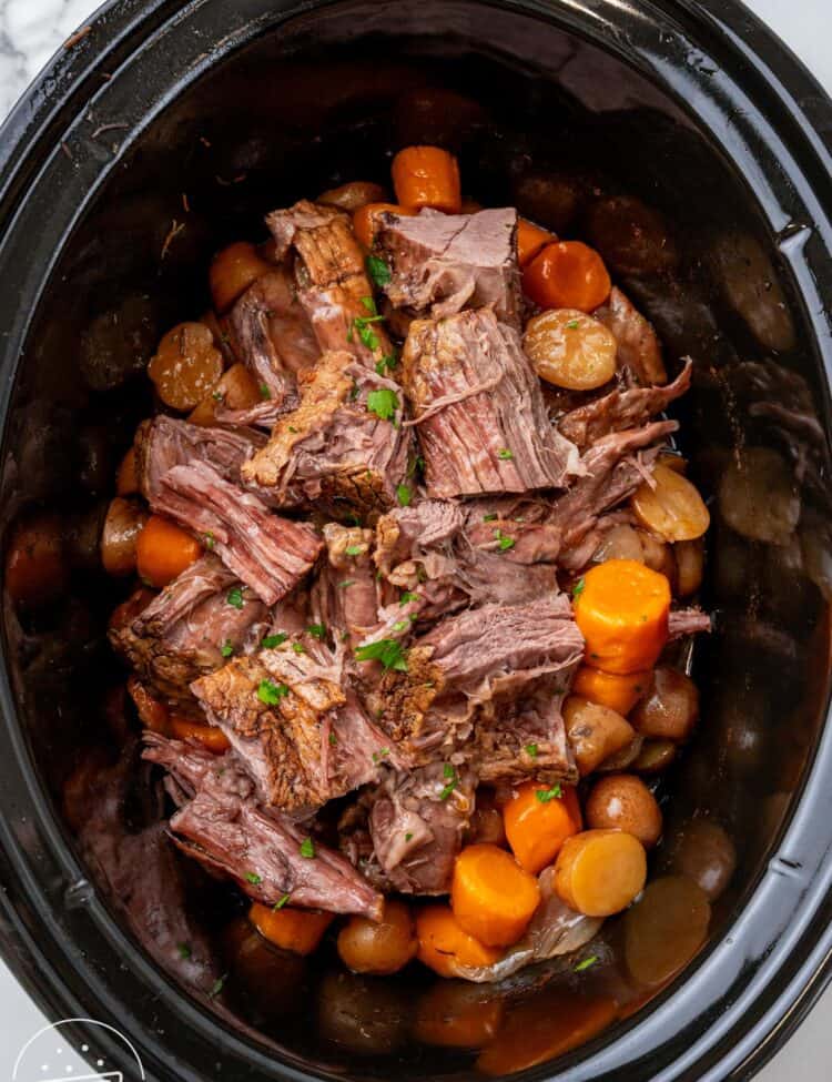 overhead view of pot roast cooked in a black oval slow cooker.