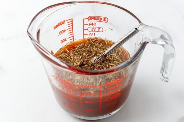 broth, tomato paste, dried herbs whisked together in a glass measuring cup with a small whisk.