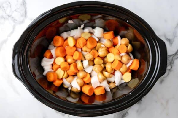 baby potatoes, thickly sliced carrots, and diced onions mixed together in a black oval crockpot.