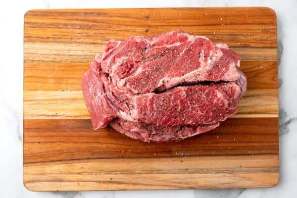 a 3 pound chuck roast on a wooden cutting board, seasoned with salt and pepper.