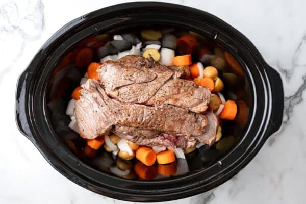 chuck roast added to a crock pot on top of vegetables.