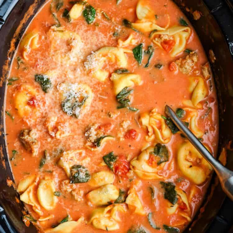 overhead view of a crockpot filled with creamy tomato broth with tortellini and spinach.