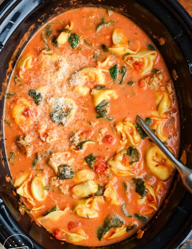 overhead view of a crockpot filled with creamy tomato broth with tortellini and spinach.