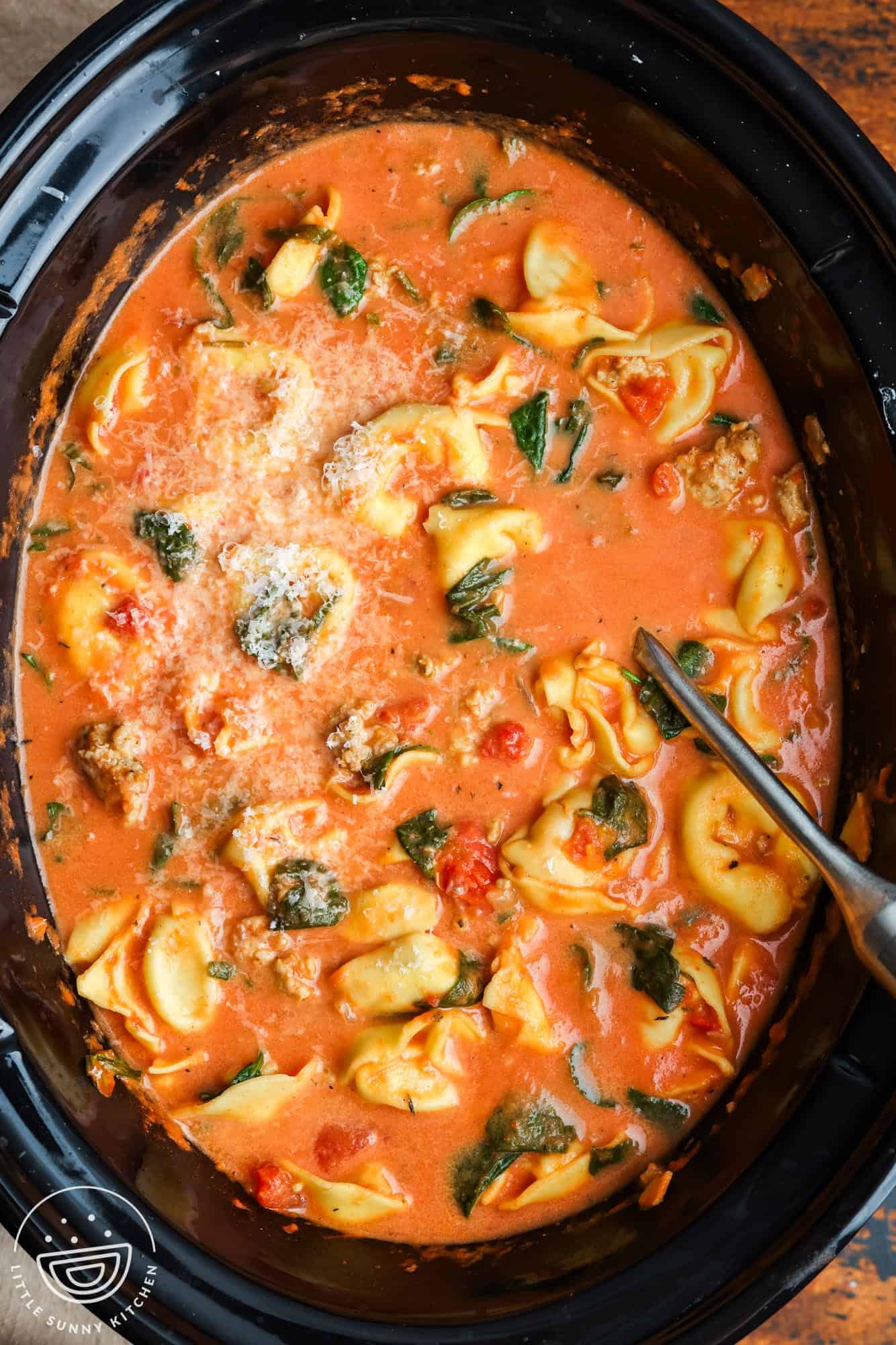 overhead view of a crockpot filled with creamy tomato broth with tortellini and spinach.