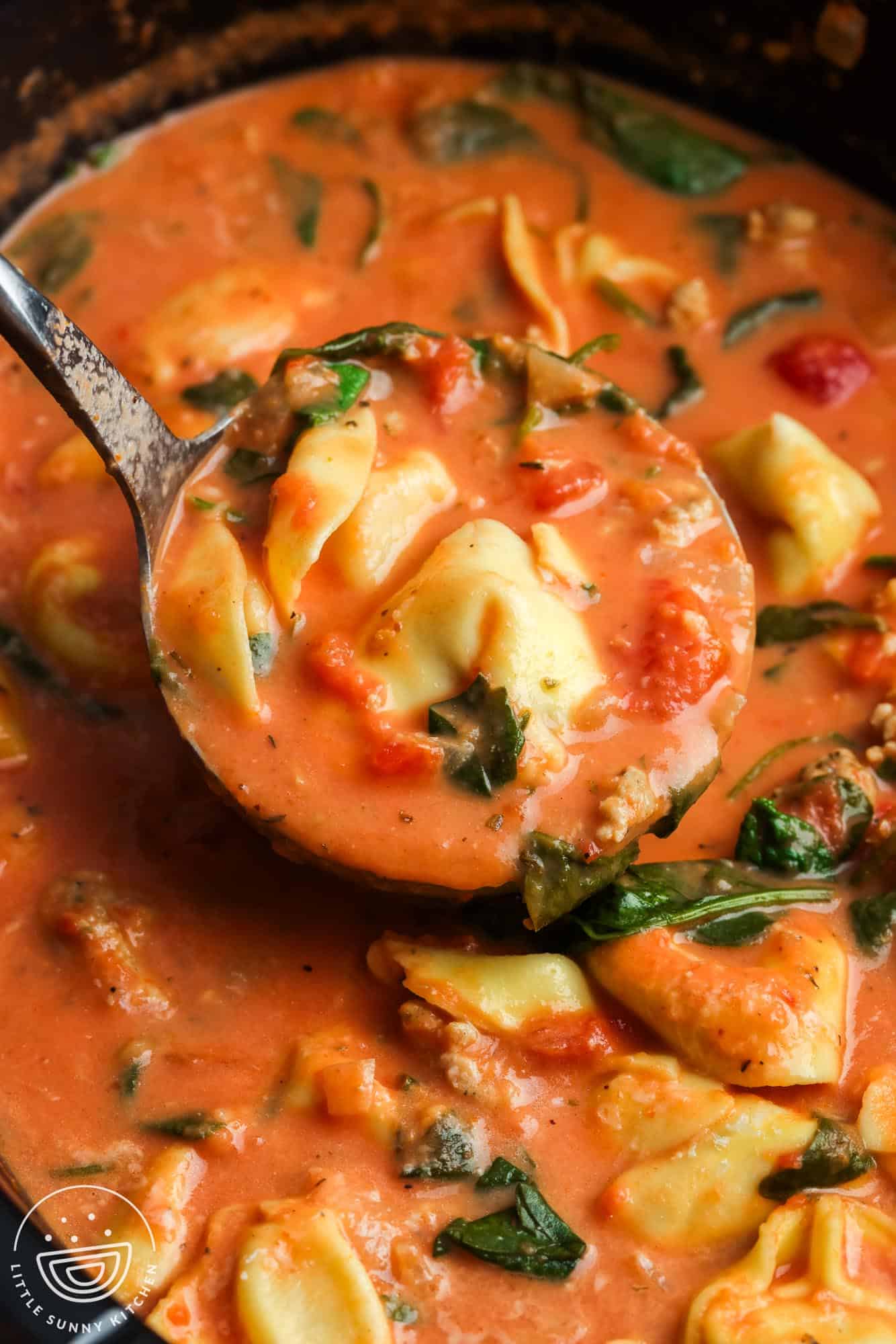 slow cooker tortellini soup served from the crock pot with a ladle.