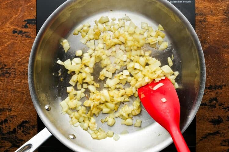 diced onions cooking in a stainless steel skillet.