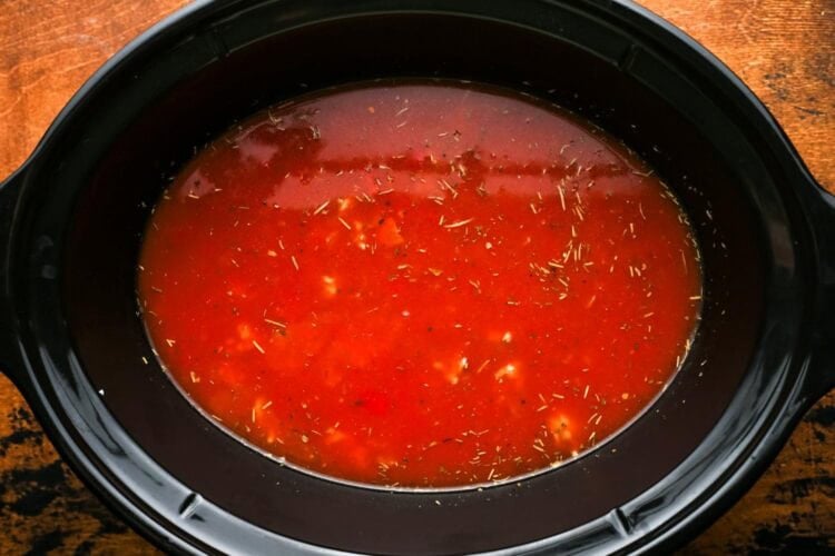 broth, tomatoes, and seasonings in a black slow cooker.