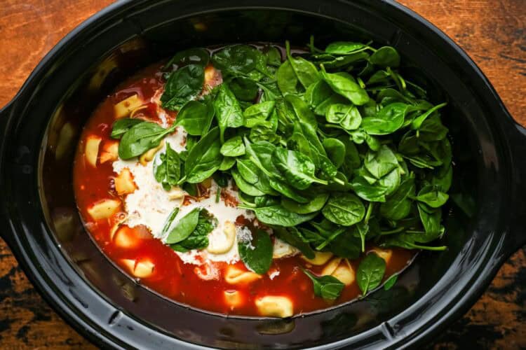 cream and baby spinach added to tortellini soup in a slow cooker.