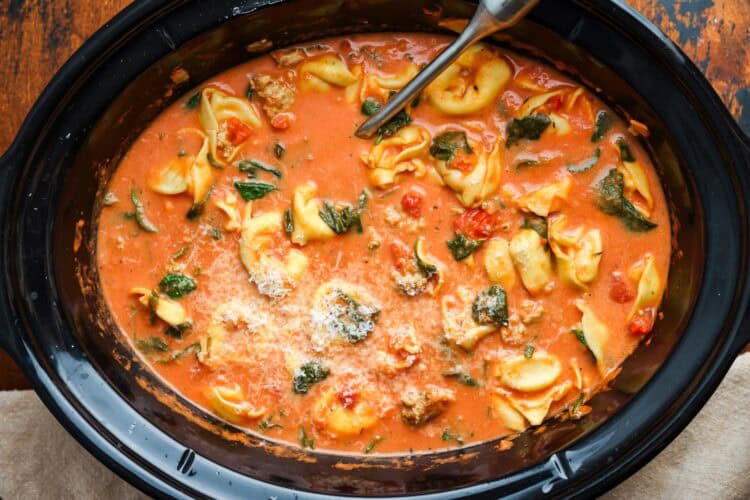 creamy tortellini soup in a slow cooker, topped with fresh parmesan cheese.