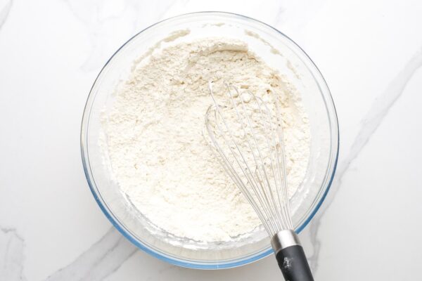 flour whisked in a glass mixing bowl, set on a marble counter.