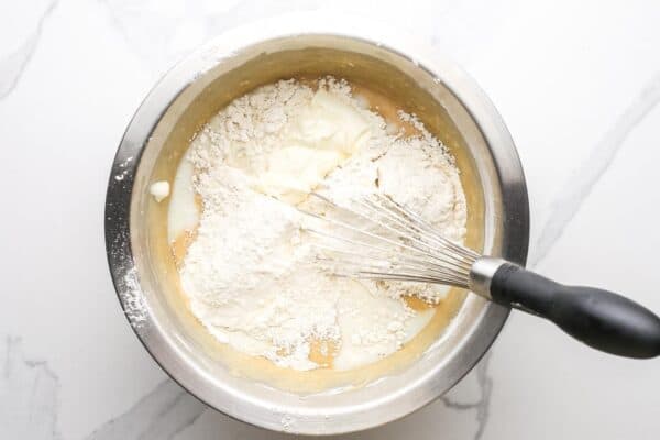 flour mixture and sour cream added to quick bread batter in a metal bowl with a whisk.