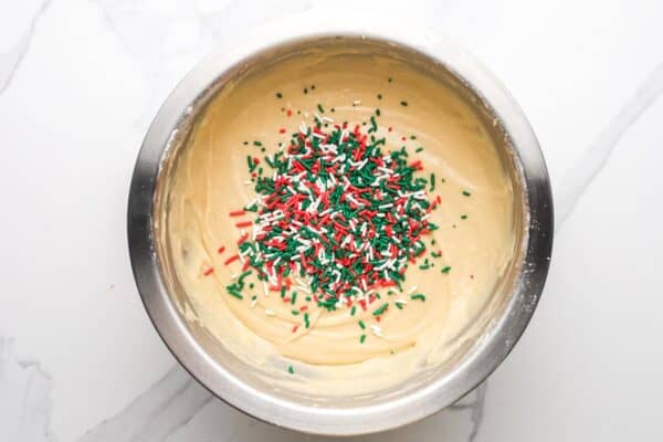 red, green, and white jimmy's added to a bowl of bread batter.