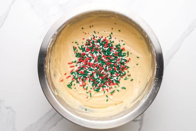 red, green, and white jimmy's added to a bowl of bread batter.