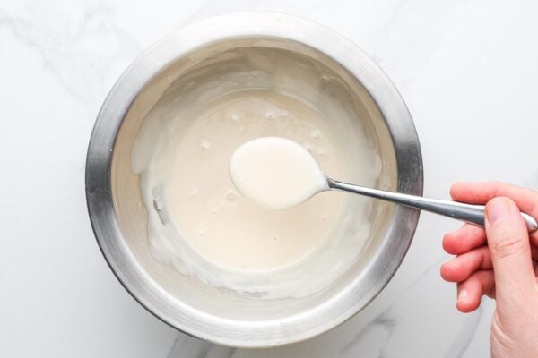 powdered sugar glaze stirred with a spoon in a metal bowl.