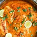 a skillet of cooked chicken with coconut lime sauce, and slices of fresh lime and cilantro for garnish.