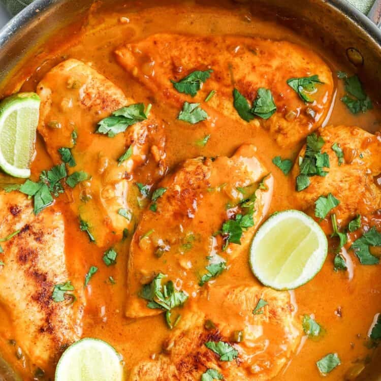 a skillet of cooked chicken with coconut lime sauce, and slices of fresh lime and cilantro for garnish.