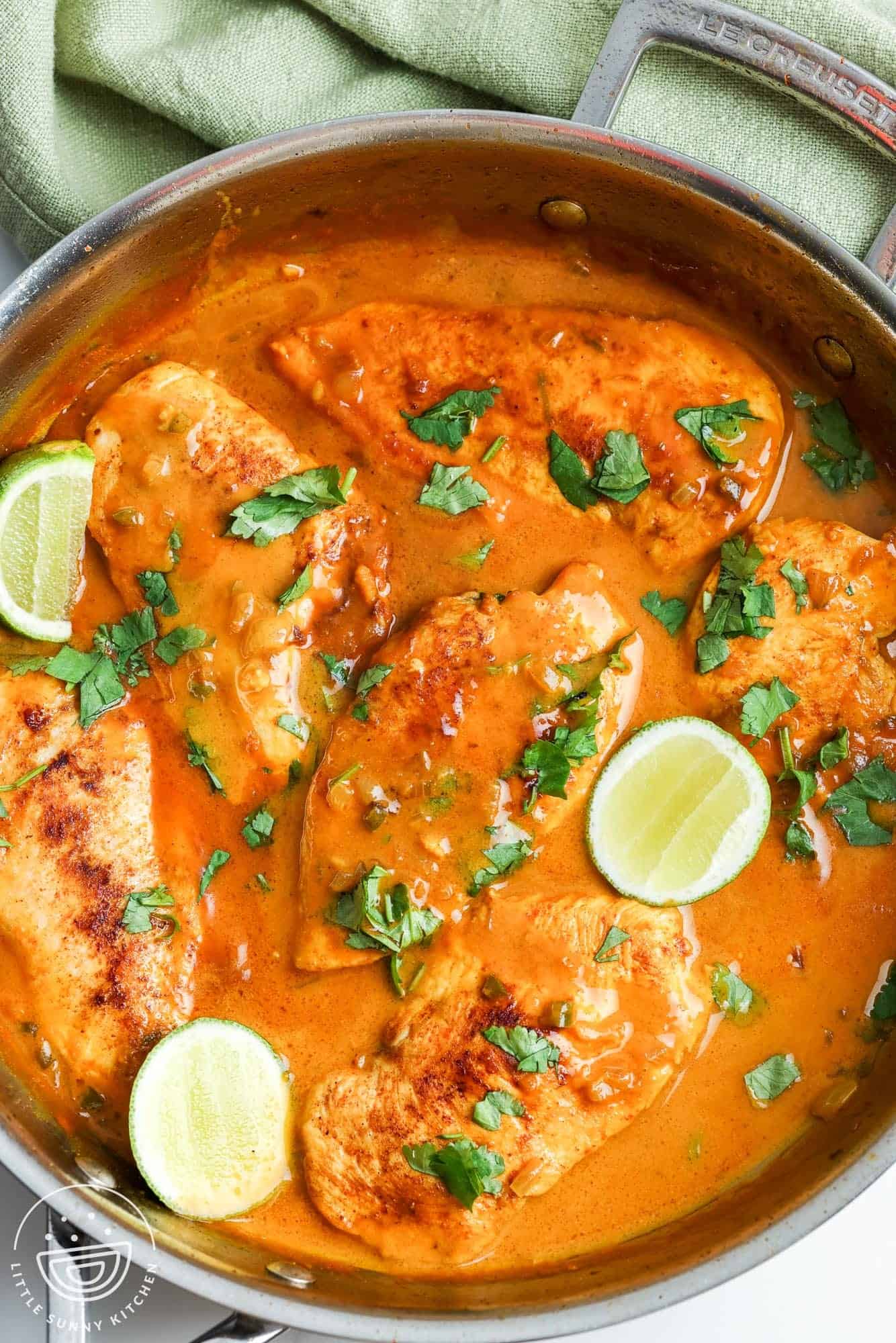 a skillet of cooked chicken with coconut lime sauce, and slices of fresh lime and cilantro for garnish.