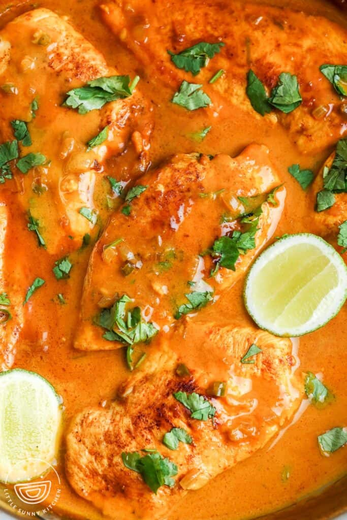 closeup of coconut lime chicken in skillet, garnished with lime wedges and chopped cilantro.