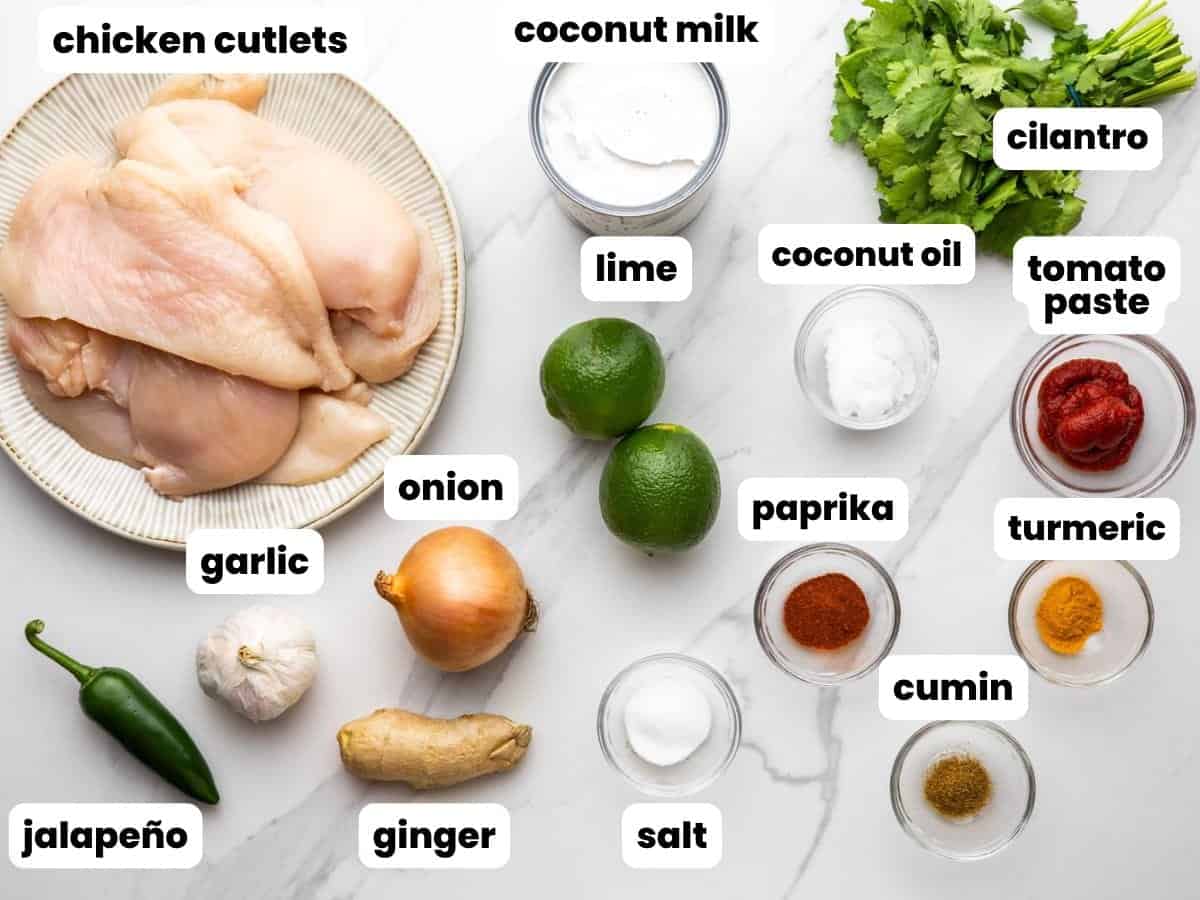 A plate of raw chicken cutlets next to the ingredients needed to make a Thai-inspired coconut lime chicken dish.