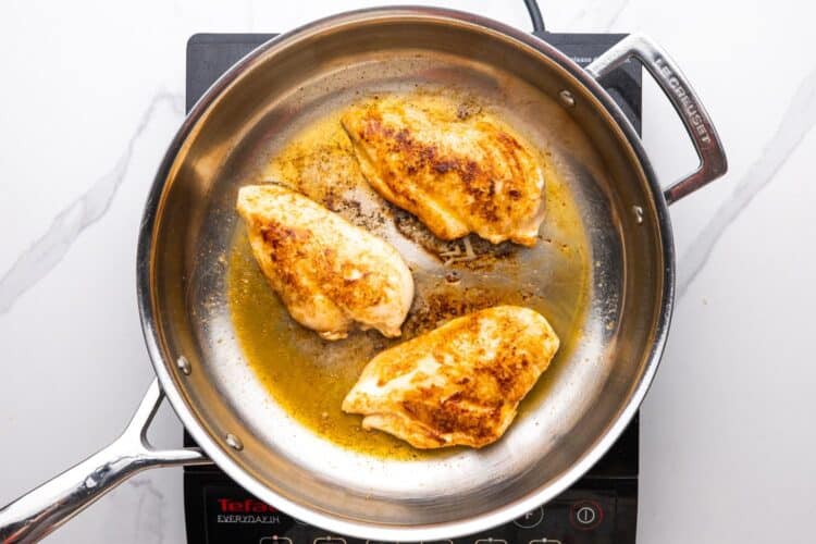 chicken cutlets cooked in a skillet with oil.