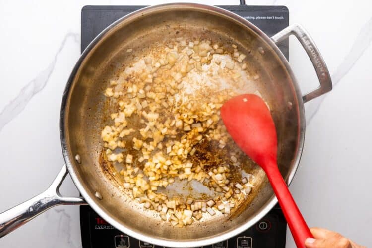diced onions sauteed in a skillet, stirred with a red spoon.