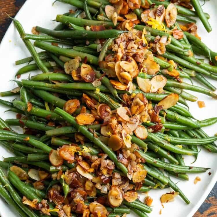 a platter of green beans almondine sitting on a wooden table.