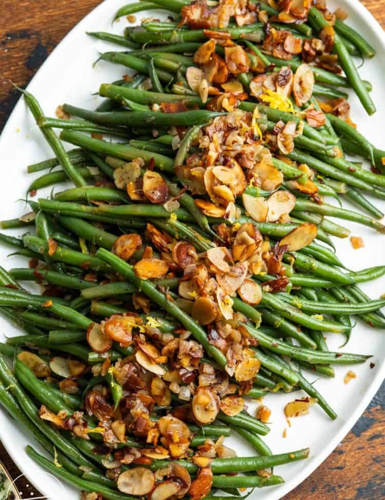 a platter of green beans almondine sitting on a wooden table.