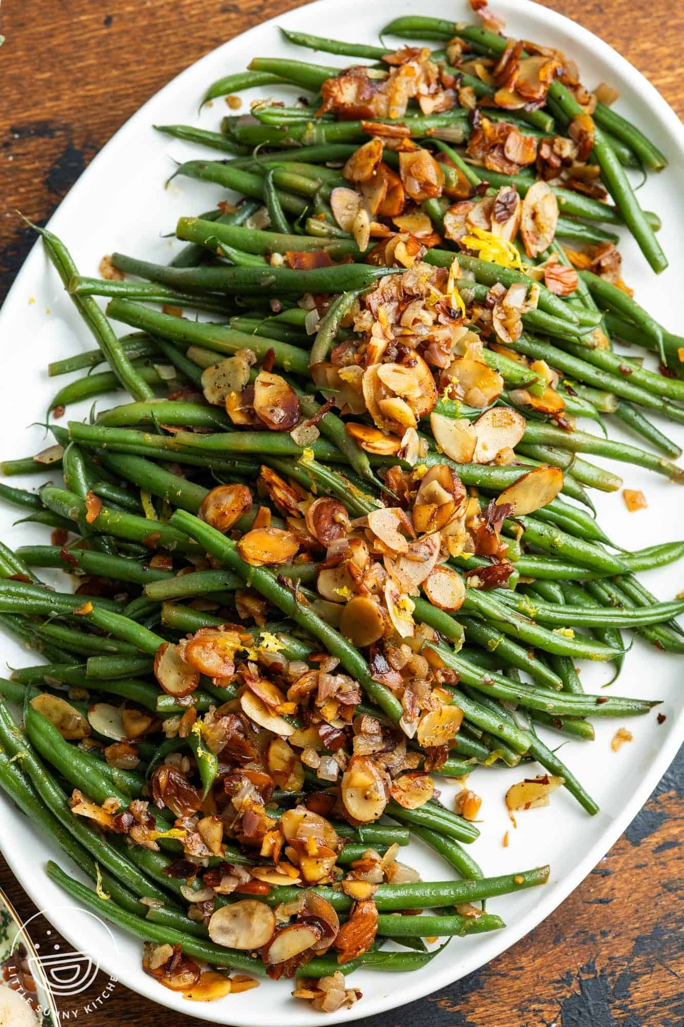 a platter of green beans almondine sitting on a wooden table.