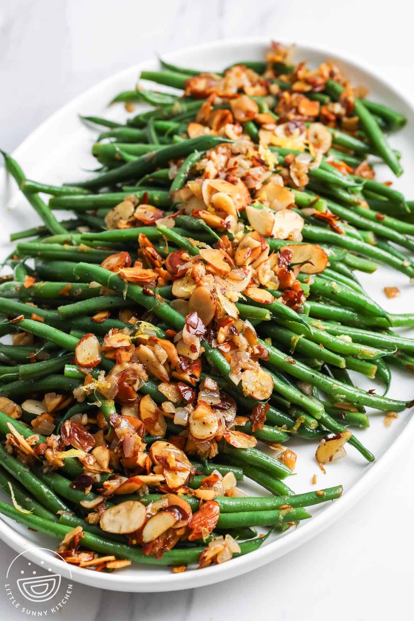 a white ceramic platter of green beans topped with toasted almonds.