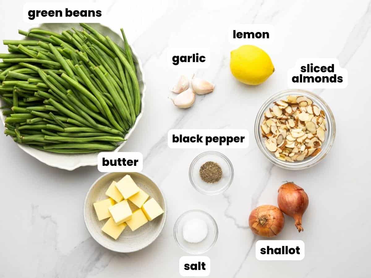 Ingredients for green beans almondine, including beans, garlic, lemon, sliced almonds, butter, and shallot.